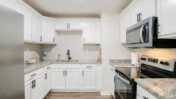 A modern kitchen with white cabinetry, a granite countertop, a stainless steel refrigerator, a microwave, and a built-in oven.