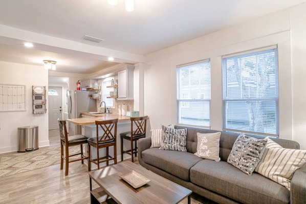A modern living room with a sofa, a dining table with chairs, and a kitchen in the background.