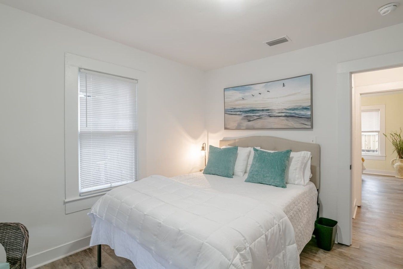 Un dormitorio con cama, ventana, un cuadro y una puerta que da a otra habitación.