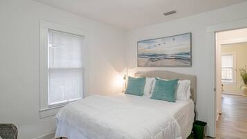 Un dormitorio con cama, ventana, un cuadro y una puerta que da a otra habitación.