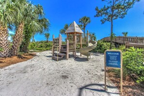 A playground with a slide and stairs, surrounded by sand and greenery, with a 'Welcome' sign. - 4309 Windsor Court North | Oceanfront 4BR Villa + Sweeping Ocean Views (Hilton Head Island)