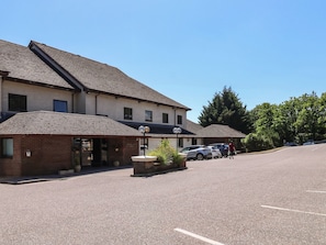 A building with a sloped roof, a brick entrance, and a parking area with cars. - Plover (Newton Abbot)