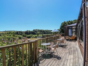 A wooden deck with outdoor seating, a glass enclosure, and a view of the countryside. - Tern (Newton Abbot)