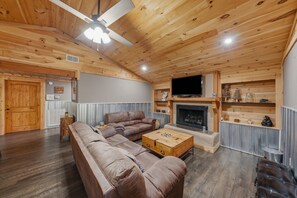 A wooden-floored living room with a sectional sofa, a television, and a fireplace. - 3BR, split residence with two hot tubs and firepit.  Great location. (Sevierville)