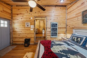 Ein gemütliches Schlafzimmer einer Holzhütte, mit einem Bett, einem Deckenventilator und einer Tür zu einem anderen Raum.