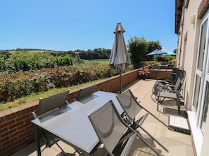 A patio area with a table and chairs, a brick wall, and a view of a field. - Avocet (Newton Abbot)