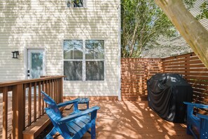 Una terraza de madera con una parrilla, una mesa de patio techada y dos sillas Adirondack.