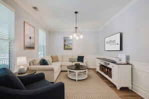 Una sala de estar moderna con un sofá, un sillón, una mesa de centro y un televisor montado en la pared.