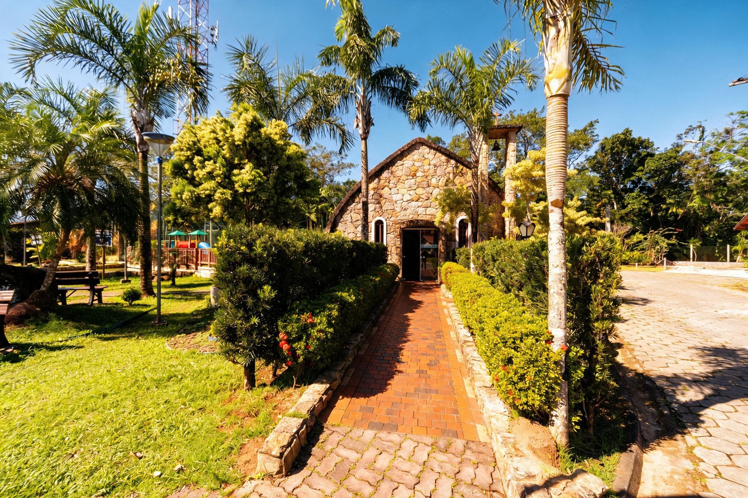 A stone building with a paved pathway leading to it, surrounded by palm trees and greenery.