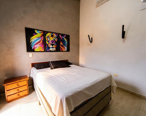 Quarto com cama, mesa de cabeceira, telefone fixado na parede e duas pinturas de leões.
