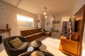 A modern living room with a sectional sofa, wicker chairs, a wooden coffee table, and a bar area with a television. - House in Morada da Praia Condominium with WiFi (Bertioga)