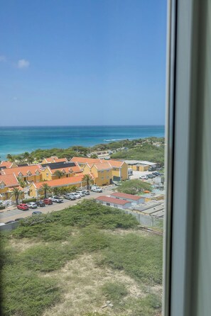 A coastal view with a row of yellow buildings, a parking area, and a clear blue sky. - A360.W62 -Atlantic Haven 1BR Penthouse (Noord)