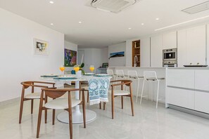 A modern kitchen with white cabinets, a built-in oven, and a dining area with wooden chairs and a round table. - A360.W62 -Atlantic Haven 1BR Penthouse (Noord)