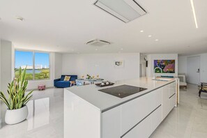 Eine moderne Küche mit einer zentralen Kochinsel, einem Essbereich mit einem blauen Sofa und Blick ins Freie.