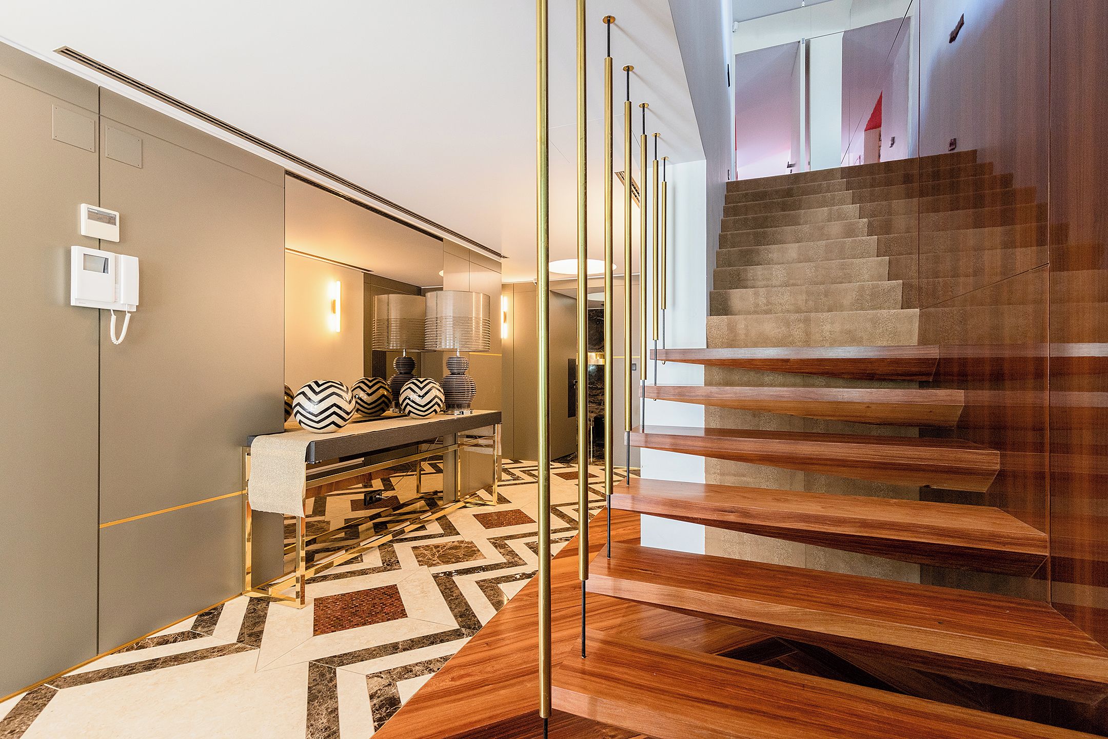 Ein modernes Interieur mit einer Holztreppe, einem gemusterten Boden und einem Spiegel, der den Raum reflektiert.