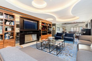 Un salon moderne doté d’un téléviseur à écran plat, de bibliothèques, d’une cheminée et d’un tapis bleu à motifs.