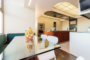 Une cuisine moderne dotée d’appareils électroménagers en acier inoxydable, d’un îlot central en bois et d’une table à manger en verre avec des chaises.