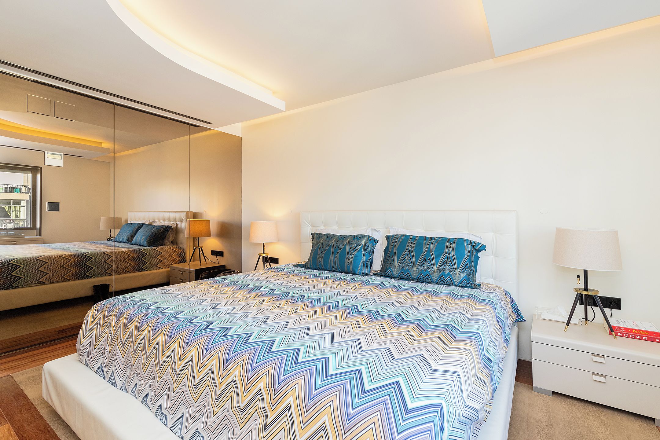Una camera d'albergo con un letto grande, un letto più piccolo e un comodino con una lampada.