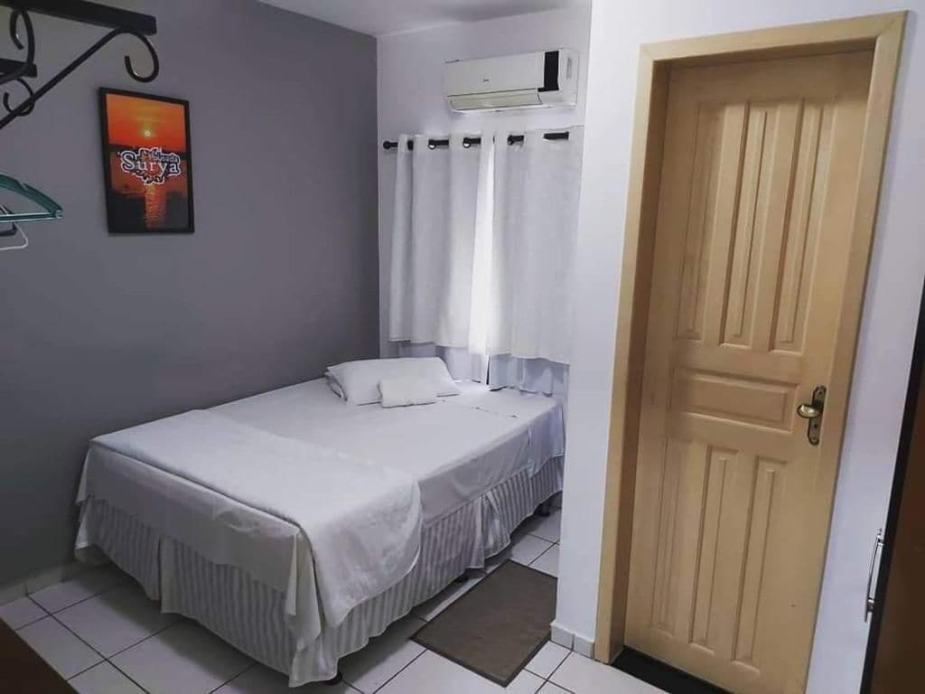 Habitación con cama individual, cubrecama blanco, una puerta y un equipo de aire acondicionado instalado en la pared.