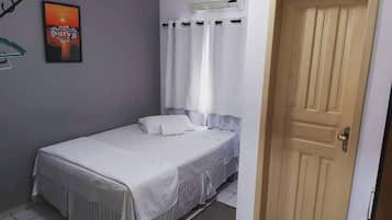 Habitación con cama individual, cubrecama blanco, una puerta y un equipo de aire acondicionado instalado en la pared.