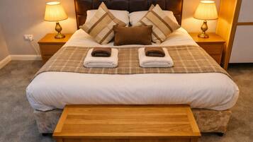 A neatly made bed with two towels, a headboard, bedside lamps, and a wooden nightstand.