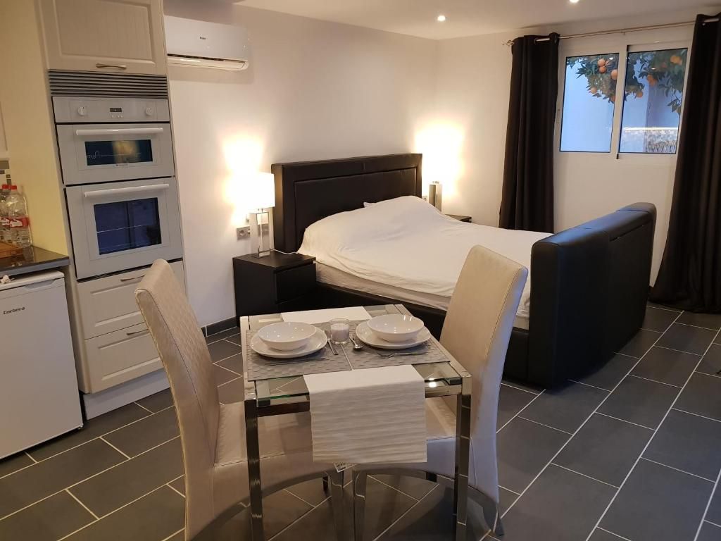 Quarto de hotel com cama, mesa de jantar com cadeiras, pequeno espaço de cozinha e janela com cortinas.