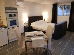 Habitación de hotel con cama, mesa de comedor con sillas, una pequeña kitchenette y ventana con cortinas.