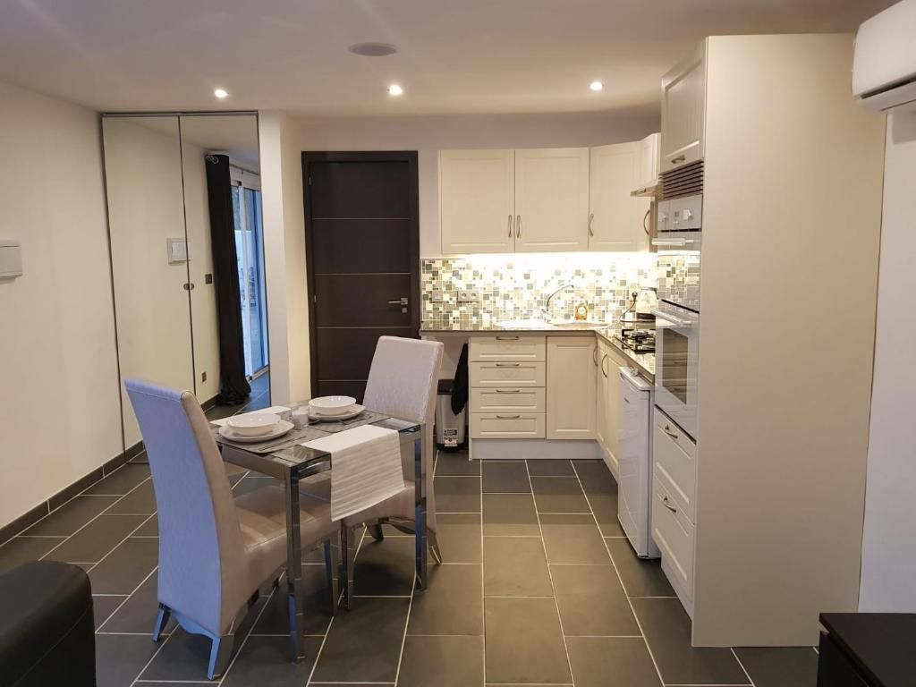 Una cocina compacta con armarios blancos, salpicadero de azulejos y una zona de comedor con mesa y sillas.