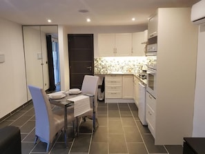 Una cocina compacta con armarios blancos, salpicadero de azulejos y una zona de comedor con mesa y sillas.