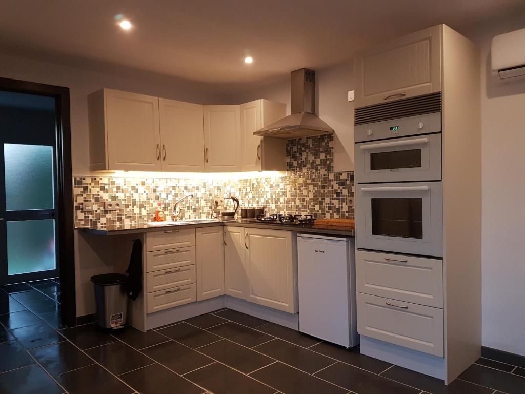 Una cocina moderna con gabinetes blancos, salpicadero de azulejos, horno empotrado y lavavajillas.