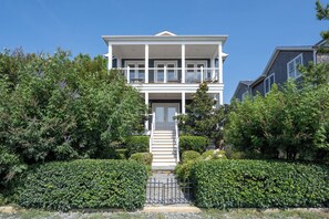 A two-story house with a front porch, a staircase leading to the entrance, and a well-maintained garden with hedges. - Beautiful home super close to the beach!  223 Grey Plover (Lewes)