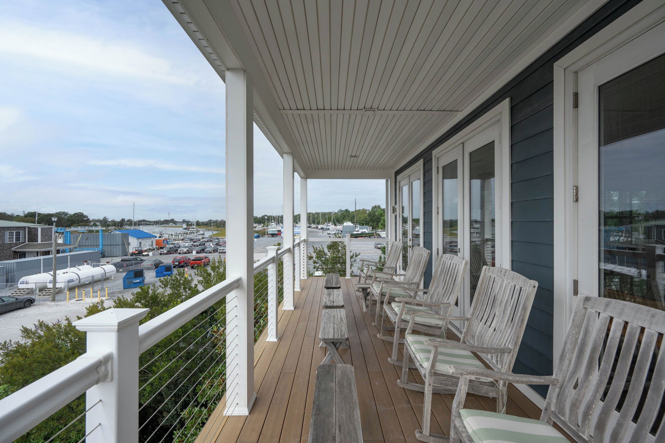 A covered outdoor area with wooden deck, white railings, and several chairs.