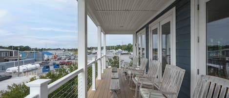 A covered outdoor area with wooden deck, white railings, and several chairs.