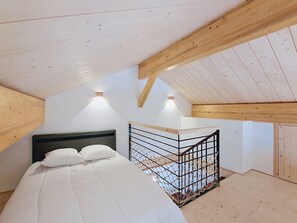 Ein Schlafzimmer mit einem Bett, einer Holzbalkendecke und einem kleinen Balkon mit Geländer.