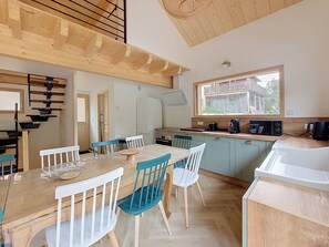 A modern kitchen with a dining area, wooden ceiling, and a view of a building outside. - Chalet des Filles -  7/9 peoples (Saint-Jean-d´Aulps)