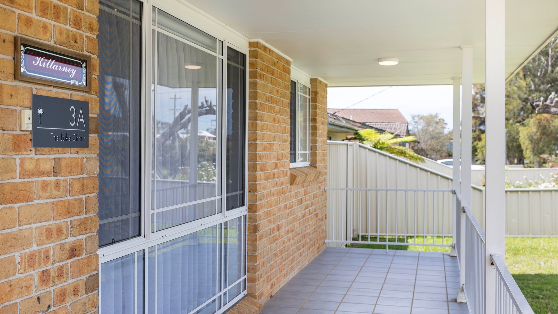 A brick building with large windows, a sign for 'Killarney 3A The Lake Circuit', and a covered porch area.