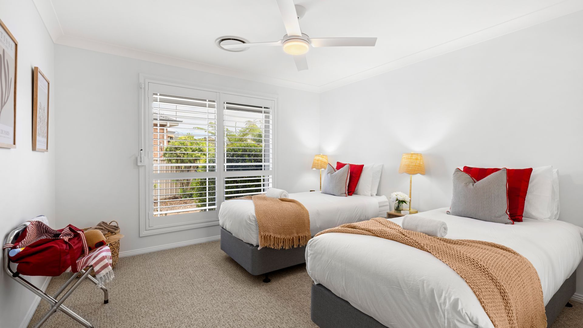 A hotel room with two beds, a ceiling fan, a window with blinds, and a luggage rack.