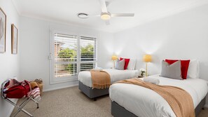 Ein Hotelzimmer mit zwei Betten, einem Deckenventilator, einem Fenster mit Jalousien und einem Gepäckträger.