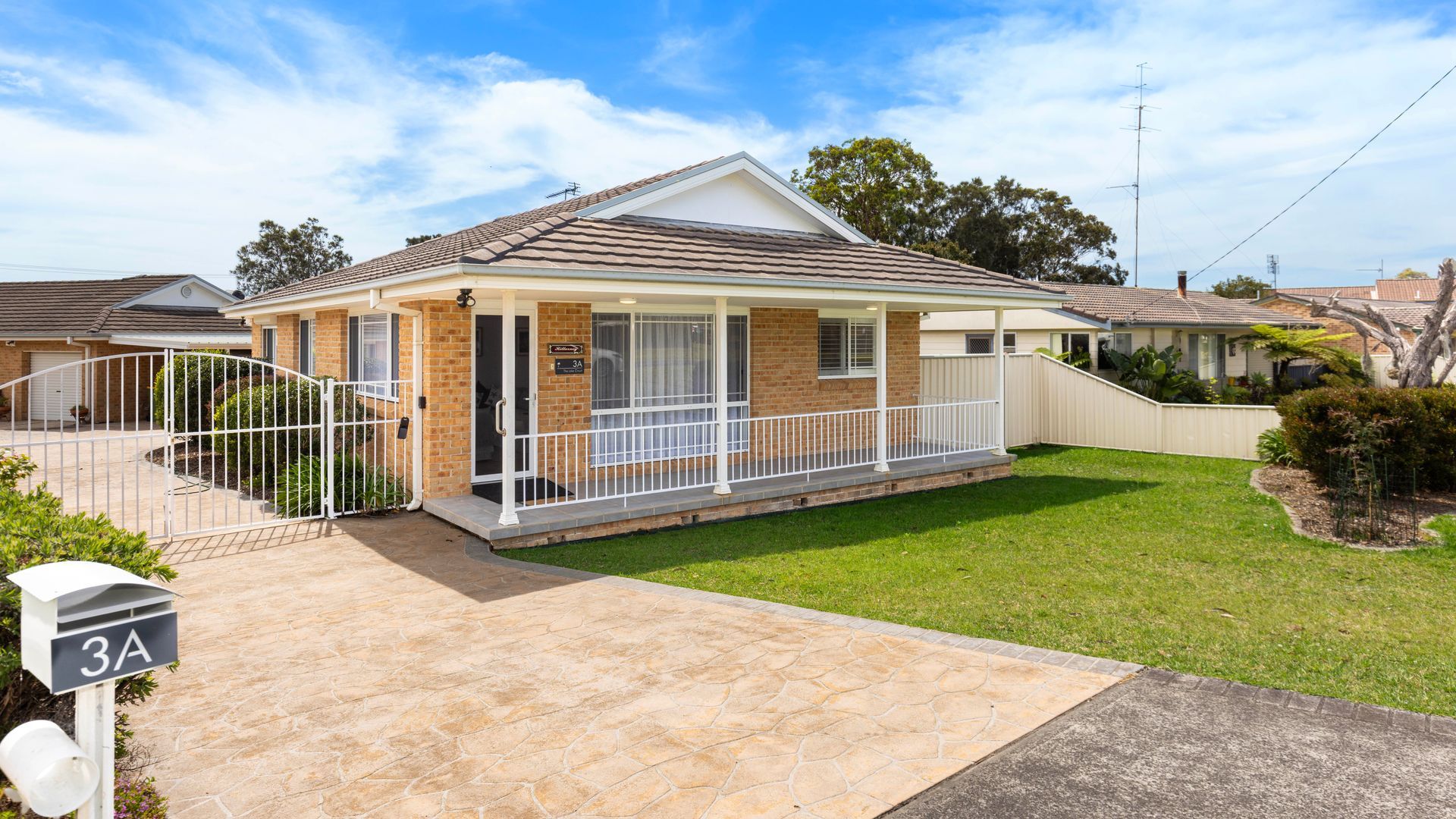 A single-story house with a covered porch, a fenced driveway, and a well-maintained lawn.
