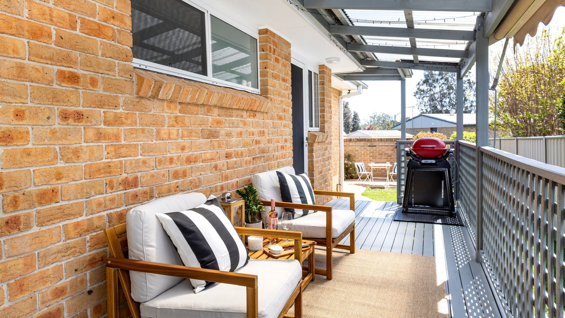 A covered outdoor seating area with a brick wall, a grill, and a view of the backyard.