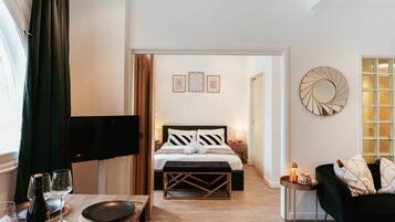 Ein Hotelzimmer mit einem Bett, einem Esstisch mit Weingläsern, einem Fernseher und einem schwarzen Sofa.