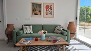 A living room with a green sofa, a coffee table with books and a vase of flowers, and two wall-mounted artworks.