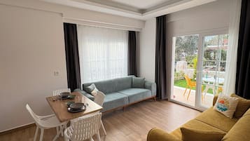 A modern living room with a sofa, a dining table with chairs, and a large window with curtains.