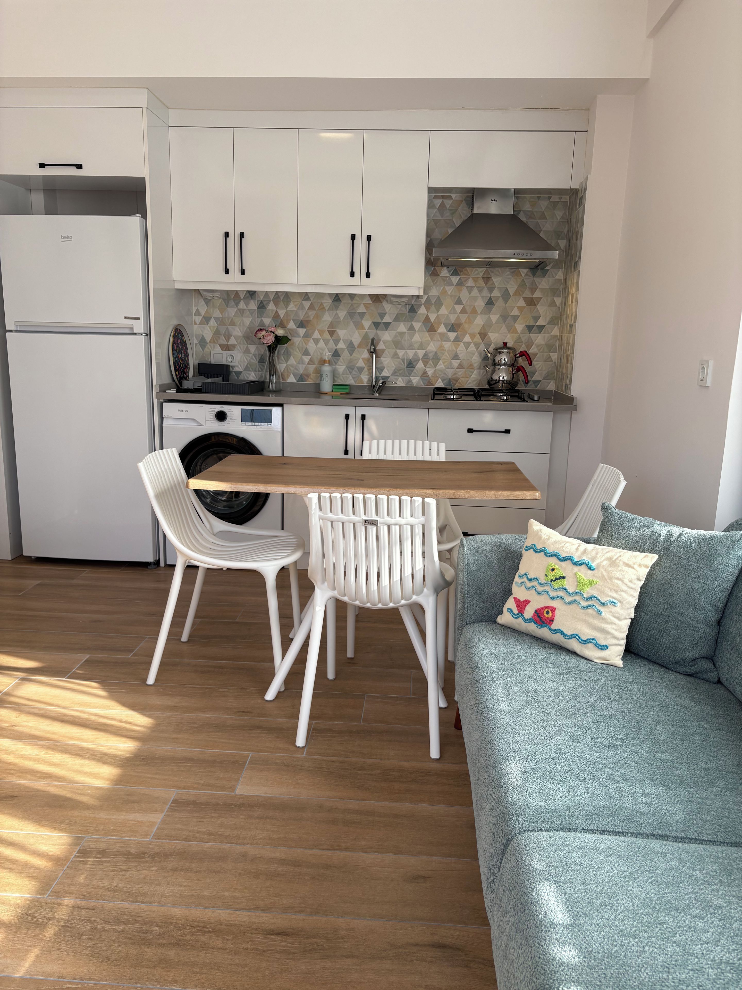 Ett kompakt kök med en matplats, en tvättmaskin och en soffa med en dekorativ prydnadskudde.