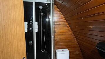 A compact bathroom with a shower enclosure, a toilet, and a wooden wall.
