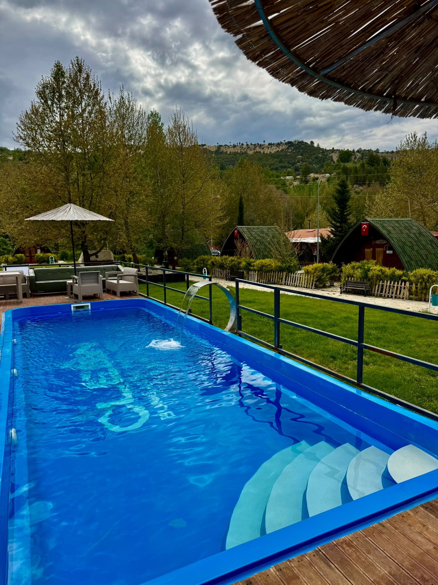 Una piscina con tobogán acuático, rodeada de mobiliario de exterior y vistas a un paisaje montañoso.