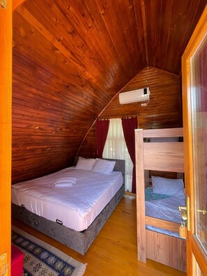 A cozy attic bedroom with a bunk bed, a single bed, wooden walls, and an air conditioning unit.