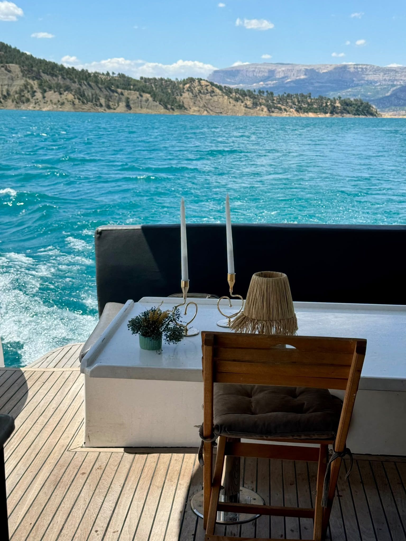 Una terraza con zona de estar frente a un cuerpo de agua, una vela y una pequeña planta.