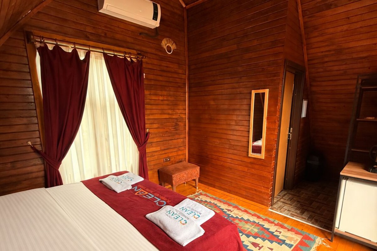A wooden cabin room with a bed, a small table, a chair, and a ladder.