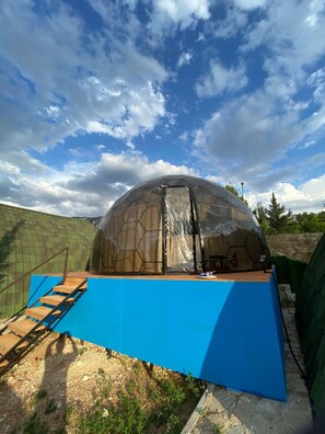 A geodesic dome structure with a staircase leading up to it, surrounded by a fenced area.